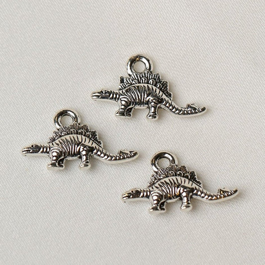Three silver-toned Stegosaurus Metal Charms (3pcs) (MLB-073) shaped like stegosauruses with loops for hanging.