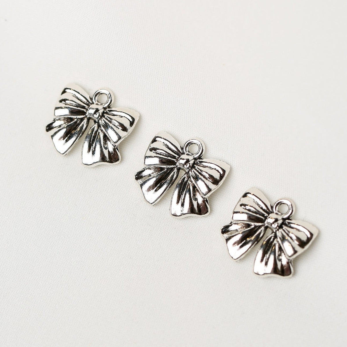 Three identical Bow Metal Charms (3pcs) (MLB-086) in a silver-toned metal, each featuring a small loop at the top.