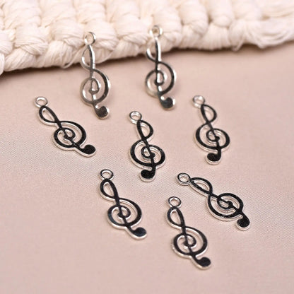 Eight Musical Clef Metal Charms (8pcs) (MLB-075) silver-toned treble clef music note charms arranged on a textured surface.