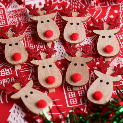 The Printable Heaven Rudolph And Red Nose Clips 8 Pack (XMA4027) features festive wooden reindeer with red noses and antlers, arranged on a red and white background with buildings, trees, and green tinsel—ideal for Christmas crafts.