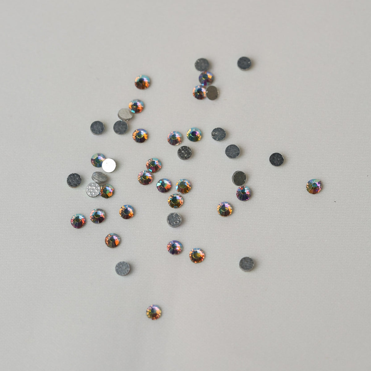 A collection of small, iridescent SS10 Hot Fix Silver Foiled AB Crystals by Printable Heaven scattered on a light surface.