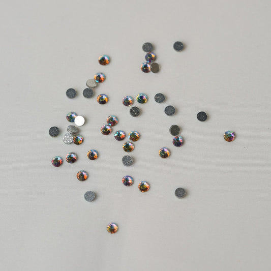 A collection of small, iridescent SS10 Hot Fix Silver Foiled AB Crystals by Printable Heaven scattered on a light surface.