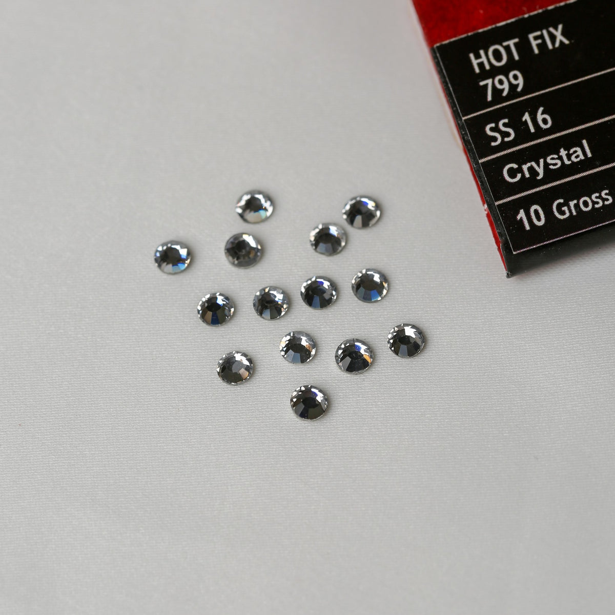 Twelve circular SS16 Hot Fix Silver Foiled AB Crystals from Printable Heaven displayed next to a box labeled Hot Fix 799 SS 16 Crystal 10 Gross.