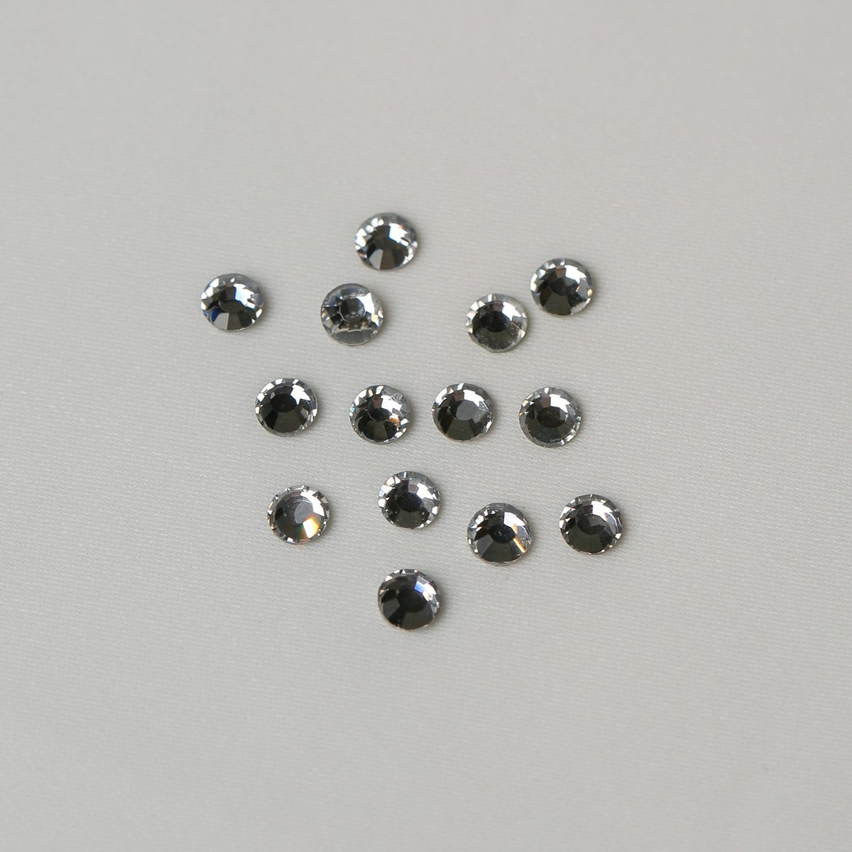 Twelve small, round, faceted SS16 Hot Fix Silver Foiled AB Crystals arranged in a loose cluster on a light grey background.