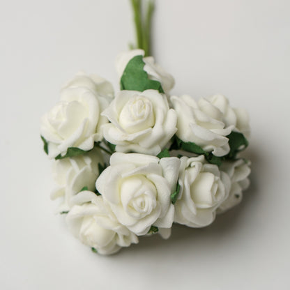 A bunch of Printable Heaven Small Foam Rose Bunch in Ivory (1″ Wide) artificial roses with green leaves on a plain background.