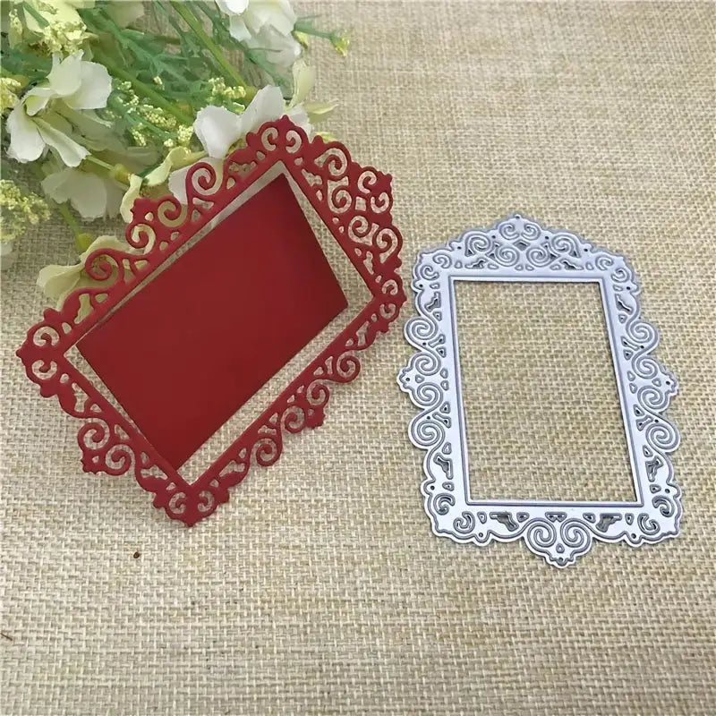 Two ornate rectangular frames, created with the Printable Heaven Ornate Decorative Frame Cutting Die (1 PC) (T048), one in red and one in silver, featuring intricate swirling patterns, are placed on a burlap surface beside white flowers.