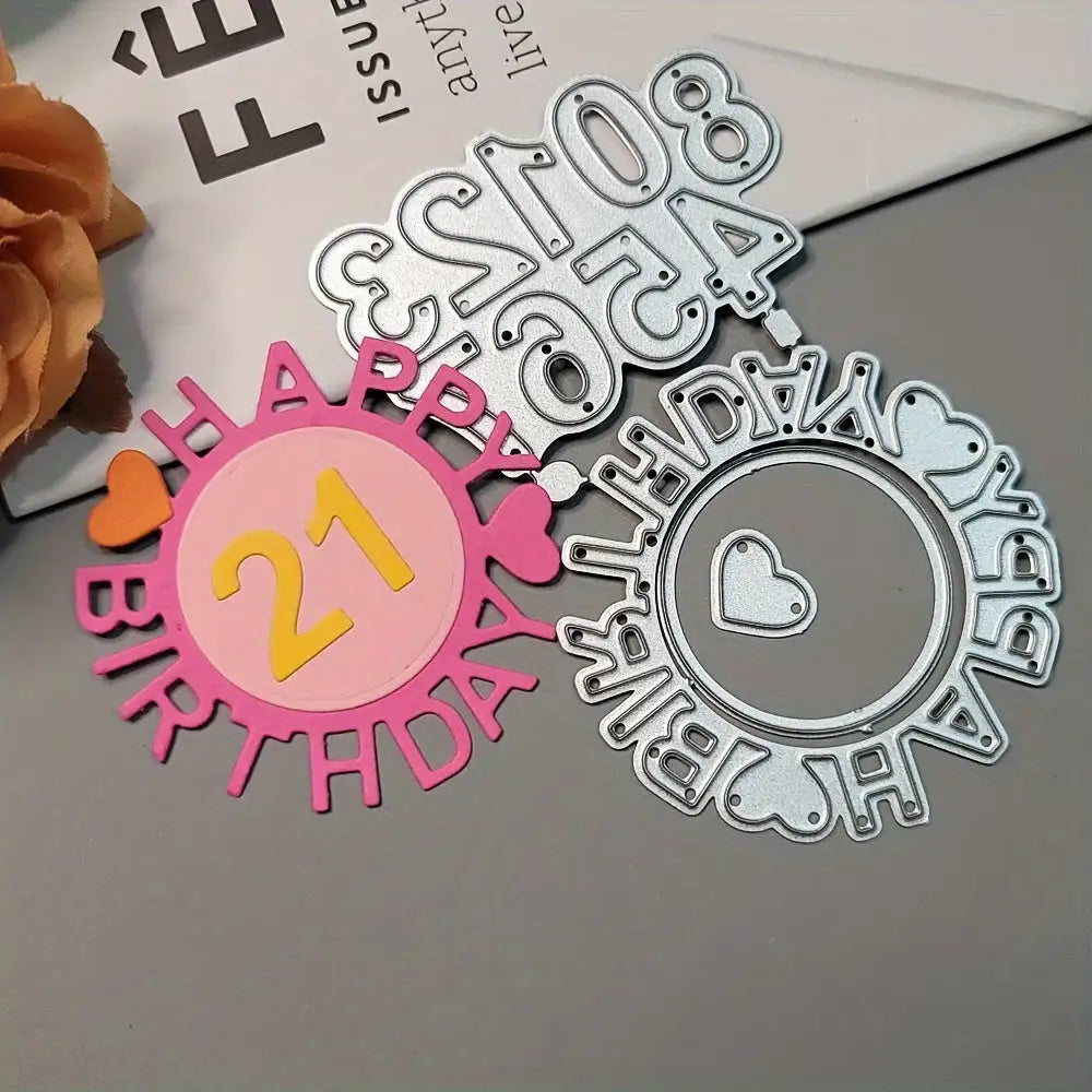 A pink and yellow “Happy Birthday 21” paper cutout with a heart, crafted using the Printable Heaven Birthday Cutting Die Set with Numbers (4 PCS) (W092), is shown next to two metal cutting dies from the same set featuring a matching circular birthday design with a heart in the center, all displayed on a gray tabletop.
