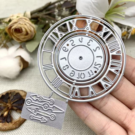 A hand displays the Printable Heaven Vintage Roman Numeral Clock, Watch Face Cutting Die (2 PCS) (D087), intricately crafted from silver paper. The circular face showcases both Roman and Arabic numerals, complemented by three individually die-cut clock hands. Ideal for paper crafts, the backdrop features softly blurred dried flowers and a pinecone.