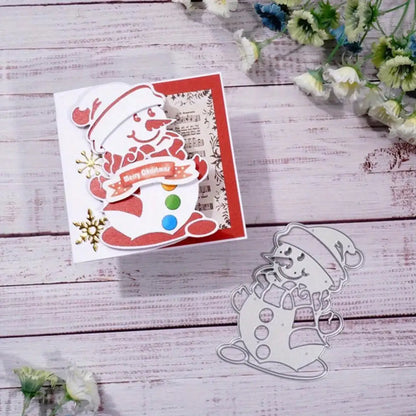 Handmade Christmas card showcasing Printable Heaven’s Snowman Christmas Cutting Die (1 PC) (P140), featuring a charming red snowman design, colorful buttons, and a festive “Merry Christmas” banner—perfect for winter-themed paper craft enthusiasts. The metal cutting die is displayed beside the card, making it an essential addition to your collection of Christmas crafts. Elegant white flowers accentuate the wooden background beautifully.